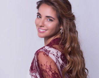 May include: A woman with long brown hair wearing a white dress with a burgundy lace shawl. The shawl has a floral pattern and is tied at the back.