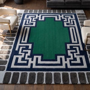 Puede incluir: Una alfombra rectangular con un rectángulo central verde sólido rodeado por un borde geométrico de estilo griego en azul marino y gris claro. El borde exterior es gris claro con bloques rectangulares gris oscuro y cuatro estrellas blancas.