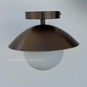 Puede incluir: Una lámpara de techo de color bronce con una pantalla redondeada y un globo de cristal esférico blanco. El accesorio está montado sobre una superficie blanca. El texto "UKFROSTLIGHTSHOPLTD" es visible.