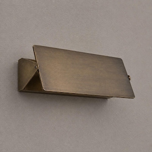 Op de afbeelding: Een rechthoekige wandlamp met een antieke messing afwerking. Het ontwerp heeft een plat, schuin voorpaneel dat uitsteekt vanaf een driehoekige zijbeugel, wat zorgt voor een strak, geometrisch profiel met een metalen, geborstelde textuur.