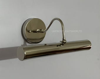 May include: A polished nickel picture light fixture. The fixture has a circular base, a curved arm, and a cylindrical light housing. The text "UKFROSTLIGHTSHOPLTD" is visible on the wall.