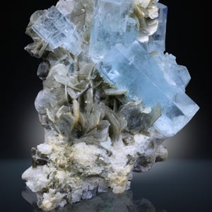 Op de afbeelding: Een cluster van lichtblauwe aquamarijnkristallen, met een glasachtige glans, tegen zilvergrijs mica. De kristallen hebben een prismatische vorm. De basis is een mix van witte en grijze mineralen. Mineraal specimen.