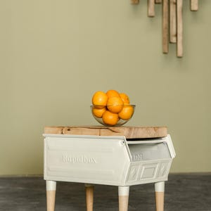 Könnte beinhalten: Ein weißes Metall-Beistelltisch mit Holzbeinen und einer Holzplatte. Auf dem Tisch steht das Wort "Rapidbox". Eine klare Glasschale mit Orangen steht auf dem Tisch.