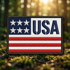 May include: Embroidered patch featuring the American flag design. The patch has a blue field with white stars, red and white stripes, and the word "USA" in blue block letters. The patch is rectangular with a black border.