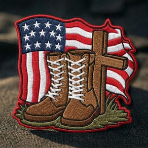 May include: Embroidered patch featuring brown combat boots with white laces, a wooden cross, and a waving American flag in red, white, and blue. The patch has a red border and is set against a dark background.