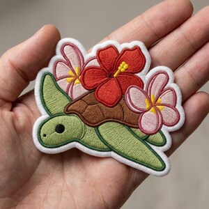 May include: An embroidered patch featuring a light green sea turtle with a brown shell. The turtle is adorned with a large, vibrant red hibiscus flower and two smaller, pale pink plumeria flowers. The entire design has a white border.