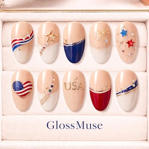 May include: A set of ten artificial nails with patriotic designs. Each nail features a nude base with white tips and various embellishments, including stars, stripes, and the word "USA". The nails are arranged in a display case.