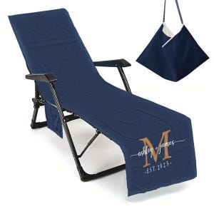 Puede incluir: Funda de silla de playa personalizada azul marino con un bolso a juego. La funda presenta una gran letra dorada "M" con los nombres "ashley + james" y la fecha "EST. 2025" impresos. La silla es negra.