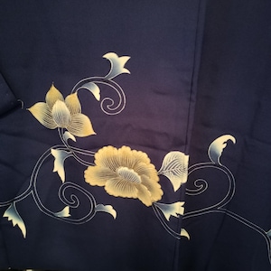 May include: Close-up of a navy blue fabric with a floral design. The design features large, yellow flowers with white and light blue accents, and white swirling vines. The fabric is folded, showing the texture and depth of the material.