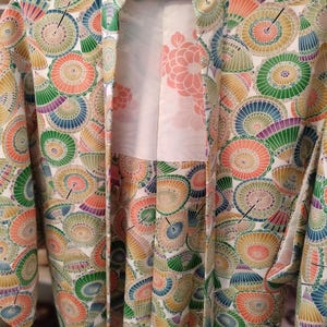 May include: A colorful kimono with a white background and a pattern of parasols in shades of orange, green, blue, and purple. The kimono's interior features a floral design in soft pink.