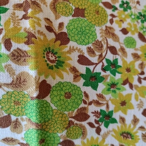 May include: A white fabric with a repeating pattern of green, brown, and yellow flowers. The fabric has a textured surface.