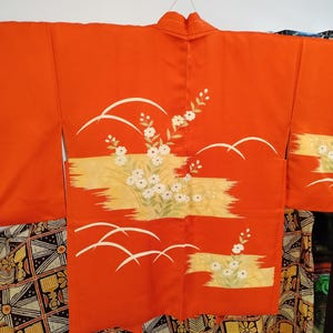 May include: A red Japanese kimono with white floral and wave designs. The kimono has a traditional style and is made of a soft, lightweight fabric.