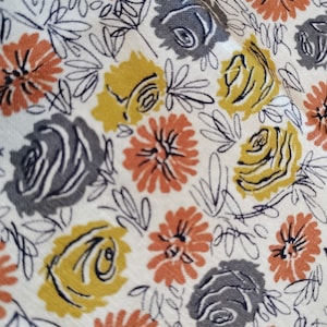 May include: Close-up of a fabric with a floral pattern. The design features stylized flowers in shades of grey, yellow, and orange, set against a cream-coloured background. Delicate black line drawings of leaves and stems complete the pattern.