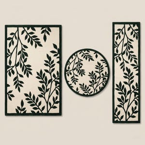 Op de afbeelding: Een set van drie vloermatten met een cr&egrave;mekleurige achtergrond en een donkergroen bladpatroon. De collectie bestaat uit &eacute;&eacute;n rechthoekige mat, &eacute;&eacute;n ronde mat en &eacute;&eacute;n lange, smalle rechthoekige loper, allemaal met een donkergroene rand.