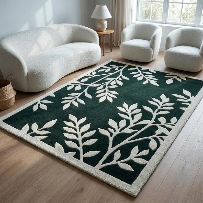 Op de afbeelding: Een rechthoekig vloerkleed met een diepgroene achtergrond en een contrasterend cr&egrave;mekleurig botanisch bladpatroon. Het ontwerp bestaat uit gestileerde takken en bladeren die over het oppervlak verspreid zijn, omlijst door een effen cr&egrave;mekleurige rand.