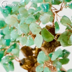 May include: A decorative tree sculpture with green gemstone leaves and copper wire branches. The trunk is a bronze color. The tree is a close-up shot, with the Lutoy C logo in the upper left corner.