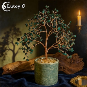 Könnte beinhalten: Eine dekorative Baumskulptur mit einem Stamm und Ästen aus Kupferdraht, verziert mit grünen Edelsteinblättern. Der Baum steht in einem hellgrünen Keramiktopf, der mit kleinen, klaren Steinen gefüllt ist. Der Hintergrund zeigt eine Kerze und eine dunkle, strukturierte Oberfläche.