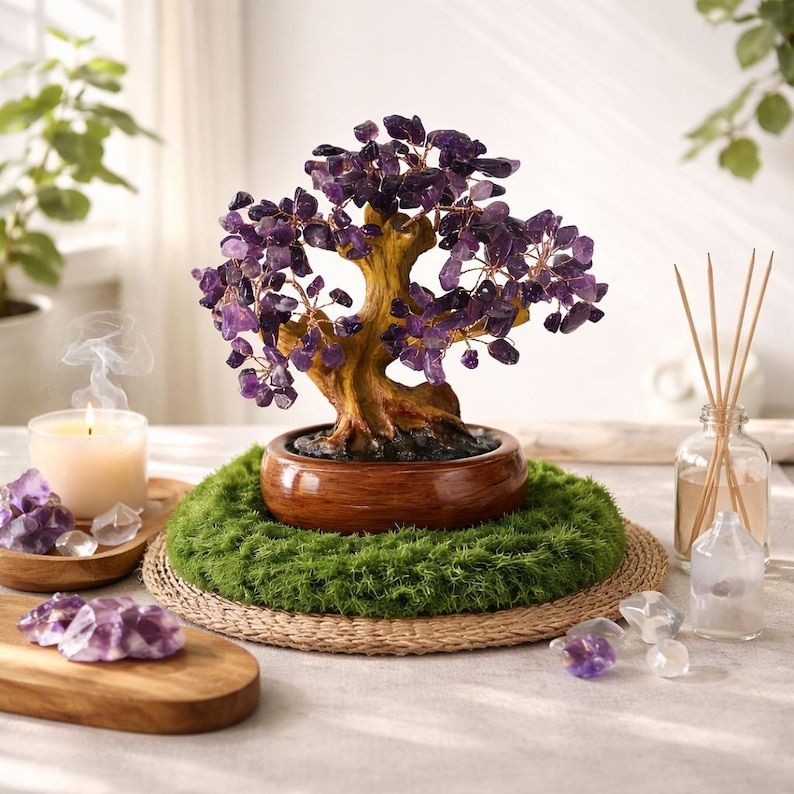 May include: A decorative amethyst gemstone tree with a brown wooden trunk and purple gemstone leaves. The tree sits in a brown pot on a bed of green moss and a woven mat. A lit candle and amethyst crystals are nearby.