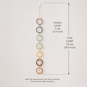 May include: A vertical hanging ornament featuring seven circular rings, each containing a clear crystal, arranged in a rainbow color sequence. The pendant length is 2.76 inches and the total length is 28.74 inches. Text indicates manual measurements.