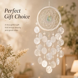 Puede incluir: Un atrapasueños blanco con un marco circular de red tejida, un dije central iridiscente en forma de lágrima y múltiples hilos colgantes adornados con discos de concha blancos y pequeñas cuentas. El texto dice: Perfect Gift Choice.