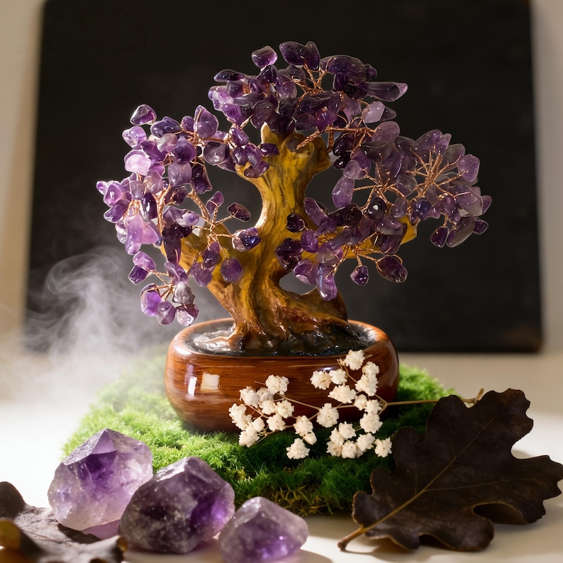 May include: A decorative amethyst crystal tree with a wooden trunk and copper wire branches, set in a small brown pot. The tree sits on a bed of green moss, with amethyst crystals and dried leaves nearby.