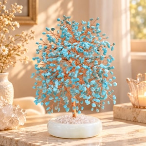 Peut inclure: Une sculpture d'arbre décorative composée de nombreuses petites pierres polies bleu vif fixées sur de fines branches en fil de cuivre flexible. L'arbre est ancré dans une base ronde en pierre blanche lisse recouverte de cristaux clairs.