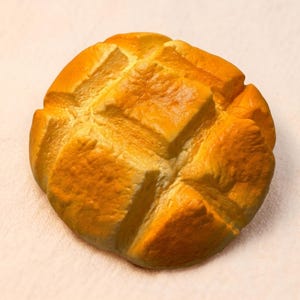May include: A golden-brown, round loaf of bread with a diamond-patterned top. The bread has a crusty exterior and appears freshly baked. The image is a close-up shot, highlighting the texture and color of the bread.