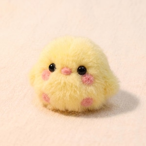 May include: A fluffy, yellow plush chick with black eyes and pink blush spots on its cheeks. The chick has a rounded body and a soft, textured appearance, giving it a cuddly look. The background is a light, neutral color.