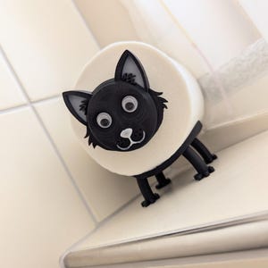 Op de afbeelding: Een grappige zeepdispenser in de vorm van een zwart-witte kat. Het gezicht van de kat is zwart met witte ogen en een kleine witte neus. De zeepdispenser heeft een ronde, crèmekleurige body en zwarte poten.