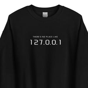 May include: Black sweatshirt with white text that reads "THERE'S NO PLACE LIKE 127.0.0.1". The sweatshirt is a solid black color and has a crew neck. The text is centered on the chest.