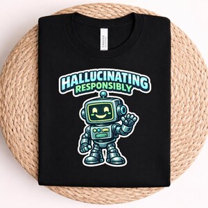 Puede incluir: Una camiseta negra con un gráfico de un robot sonriente que saluda con la mano y tiene una pantalla como cara. Sobre el robot, el texto "HALLUCINATING RESPONSIBLY" aparece en letras de color azul claro y verde. Tiene cuello redondo.
