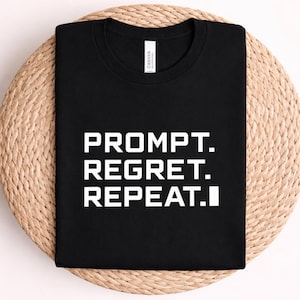Puede incluir: Una camiseta negra de manga corta con el texto blanco PROMPT. REGRET. REPEAT. impreso en una fuente sans-serif en negrita en la parte delantera. La prenda tiene un cuello redondo y una etiqueta de marca blanca visible en el interior del cuello.
