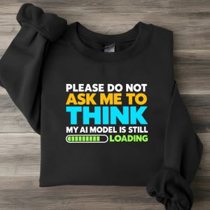 Może przedstawiać: Czarna bluza z długim rękawem z białym, żółtym i cyjanowym napisem: PLEASE DO NOT ASK ME TO THINK MY AI MODEL IS STILL LOADING, któremu towarzyszy zielono-biała grafika paska postępu.