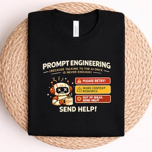 May include: A black t-shirt featuring a graphic of a sad robot holding a mug labeled CODE. The text reads PROMPT ENGINEERING (BECAUSE TALKING TO THE AI ONCE IS NEVER ENOUGH), PLEASE RETRY!, MORE CONTEXT REQUIRED, OUT OF IDEAS. SEND HELP!, and SEND HELP!