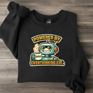 Könnte beinhalten: Ein schwarzes Sweatshirt mit Rundhalsausschnitt und einer Grafik eines lächelnden Roboters, der eine dampfende Tasse mit der Aufschrift SYNTAX hält. Der Text über dem Roboter lautet POWERED BY und darunter OVERTHINKING.EXE in fetten orangefarbenen Buchstaben.