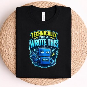Könnte beinhalten: Ein schwarzes T-Shirt mit einer Grafik eines blauen Roboters mit selbstgefälligem Ausdruck, der nach oben zeigt. Der Text über dem Roboter lautet "TECHNICALLY THE AI WROTE THIS" in gelber und blauer Schrift, umgeben von gelben Blitzen.