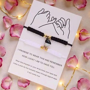 May include: Two matching friendship bracelets, one black and one white, with a heart-shaped charm. The bracelets are displayed on a card with the text "I PROMISE TO WEAR THIS AND REMEMBER HOW LUCKY I AM TO HAVE YOU."