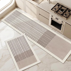 May include: A set of two rectangular kitchen floor mats featuring a cream-coloured border and a pattern of thin, dark brown vertical stripes that transition into a solid light brown block at one end of each mat, creating a clean, linear design.