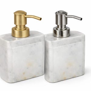 Può includere: Due dispenser di sapone rettangolari con basi in marmo. Uno ha una pompa color oro, l'altro una pompa color argento. Entrambi i dispenser hanno un beccuccio curvo per erogare sapone liquido.