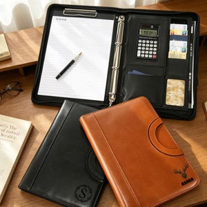 May include: Black and brown leather business portfolios with a notepad, pen, calculator, and card slots. One portfolio is open, revealing the interior. The other two are closed, one black with an "S" and one brown with a deer graphic and the name "Asher".