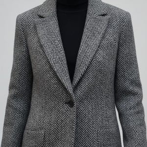 May include: A gray and white herringbone pattern blazer with a single-button closure. The blazer has a notched lapel and two front pockets. The collar is open, revealing a black turtleneck. The fabric has a textured appearance.
