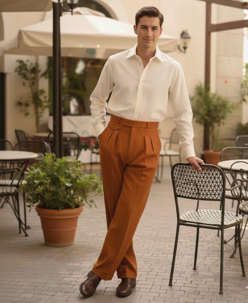 May include: A person in a white shirt and rust-coloured, high-waisted trousers with pleats. They are wearing brown shoes. The scene is set in an outdoor cafe. The trousers are a shade of brown.