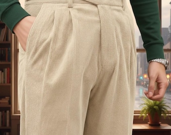 May include: Beige corduroy pants with a high waist and pleated front. The pants have a belt and pockets. The person is wearing a green long-sleeve shirt. The pants are a neutral color, suitable for various outfits.