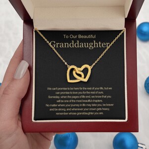 May include: A gold-toned necklace featuring two interlocking heart pendants, presented in a dark red box. The black insert displays the text: To Our Beautiful Granddaughter, followed by a sentimental message about love, life, and strength.