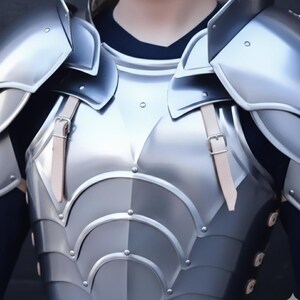 以下が含まれることがあります： 肩当て付きの銀色の金属製胸当てのクローズアップ。 アーマーは、リベットと革ストラップを備えた多層設計です。 背景は暗く、アーマーの金属的な輝きを強調しています。