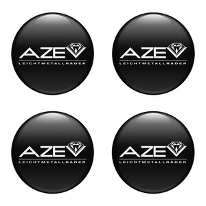 May include: A set of four circular black wheel centre caps with a glossy finish. Each cap features the white text AZEV with a diamond graphic above the letter V and the word LEICHTMETALLRÄDER printed in white underneath the brand name.