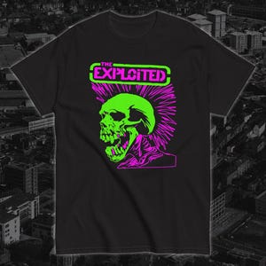 Pode incluir: Camiseta preta com uma caveira verde neon e um moicano rosa. O texto "THE EXPLOITED" está em um retângulo verde e rosa. O design é um gráfico arrojado de estilo punk rock.