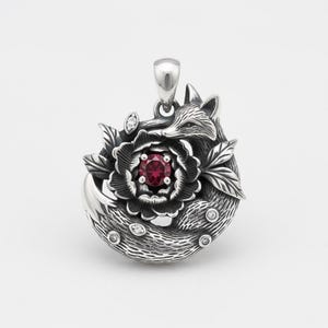 Puede incluir: Colgante de plata con un diseño de zorro que rodea una flor con un centro de piedra roja. El colgante tiene un acabado detallado y texturizado y está adornado con pequeñas gemas transparentes. La cabeza del zorro es visible en la parte superior, con la cola envolviendo la flor.