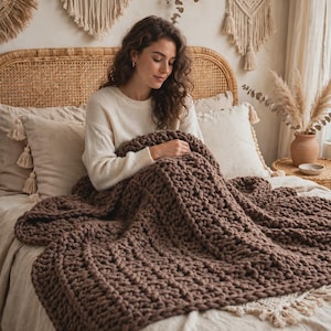 May include: A chunky knit throw blanket in a solid dark brown color featuring a thick, textured yarn construction with a repeating loop pattern. The blanket is draped over a bed, showcasing its heavy, soft, and voluminous appearance.