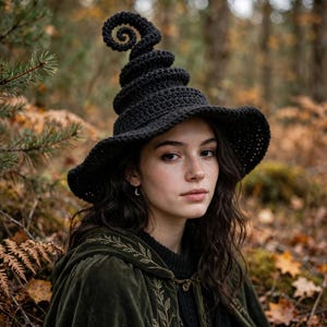 Könnte beinhalten: Ein schwarzer Häkelhut mit einer hohen, spiralförmigen, spitzen Krone und einer breiten Krempe. Der Hut zeichnet sich durch eine strukturierte Garnkonstruktion mit einem markanten, gewundenen Oberteil aus, das spitz zuläuft.